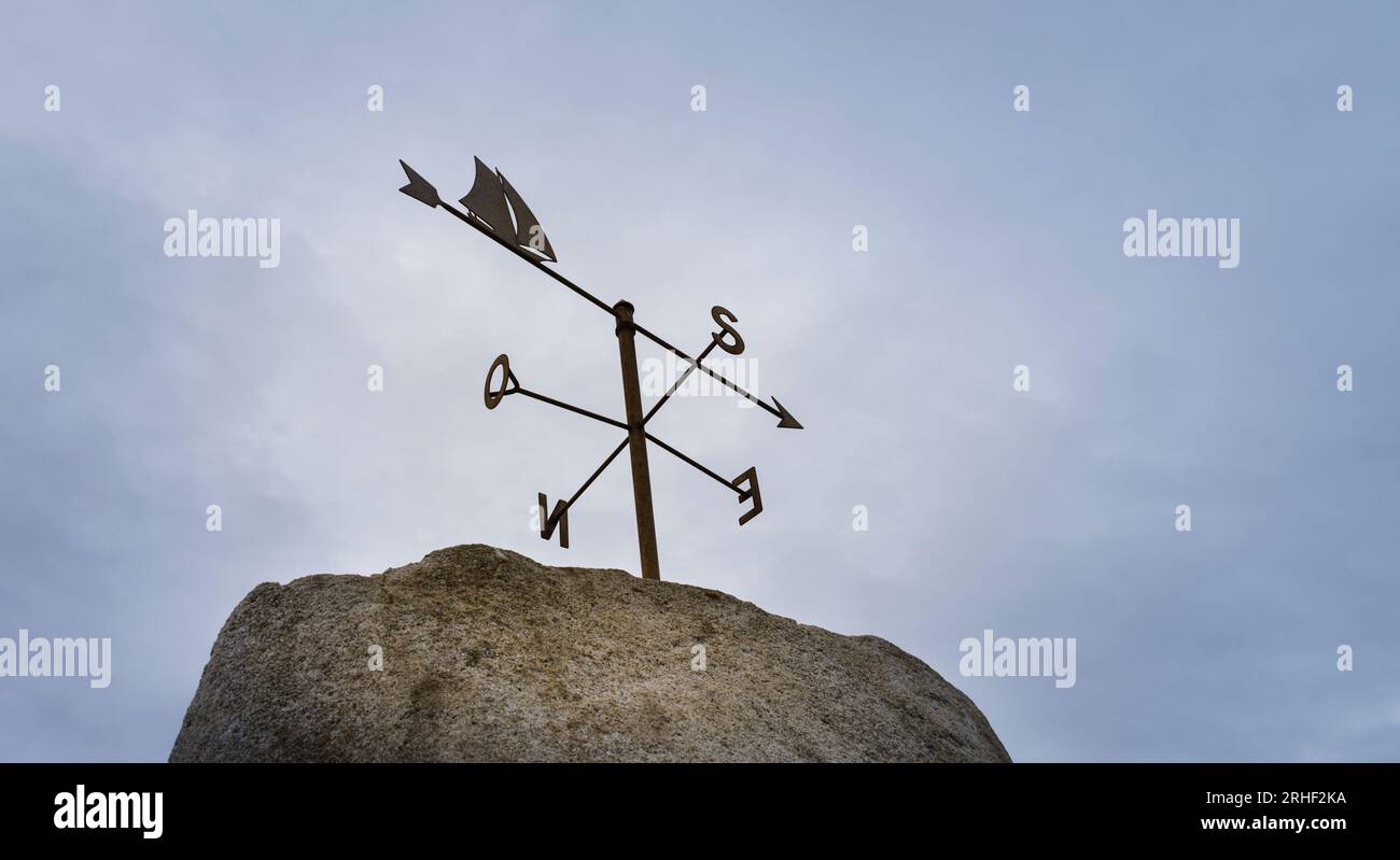 Image of a weather vane over a cloudy sky also marking the four cardinal points. Stock Photo