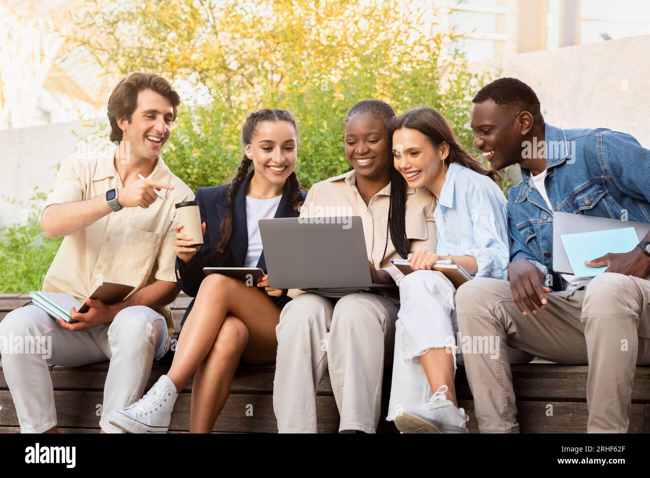 Multiracial group of students sitting on bench, using laptop Stock Photo