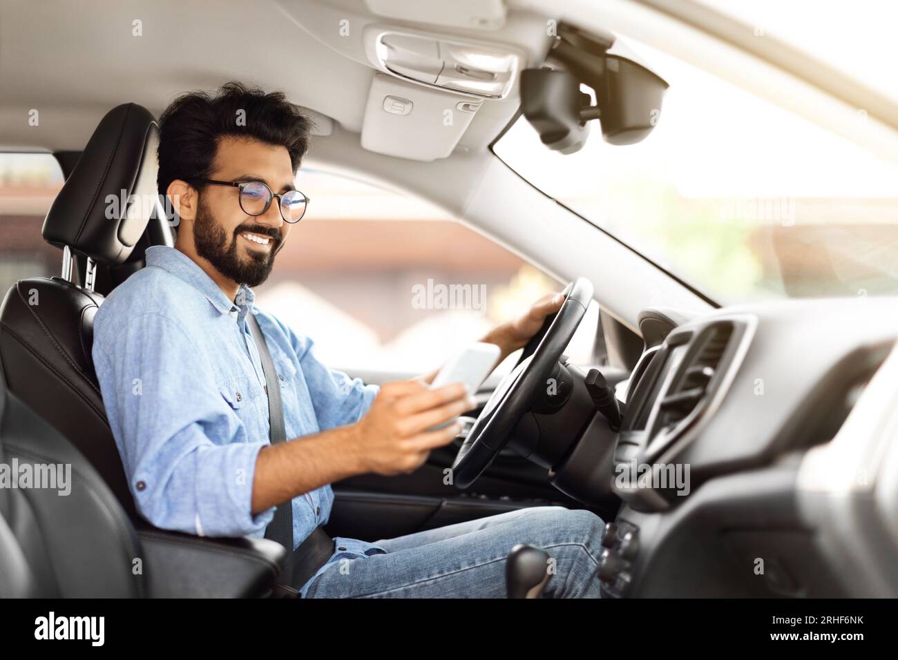 Happy young indian guy using smartphone while driving car Stock Photo