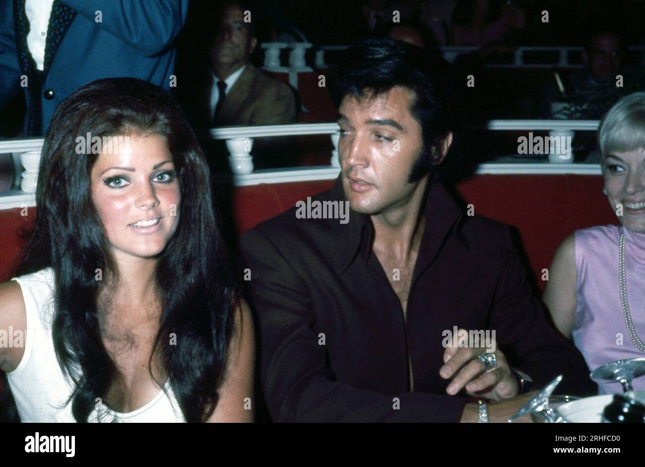 Elvis Presley wearing black, sitting at table with his wife