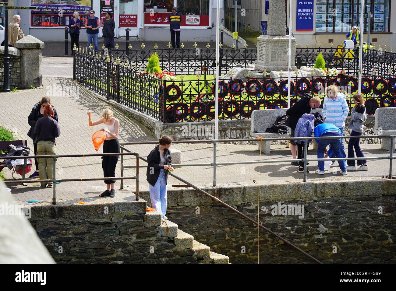 Looe, UK - August 2023: Holiday makers fishing for crab at Looe harbour and the East Looe river Stock Photo