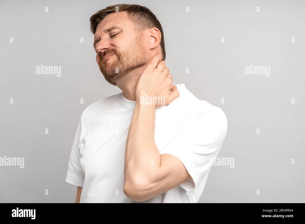 Man suffers from neck pain isolated on studio gray background. Neck ache, hernia concept Stock Photo