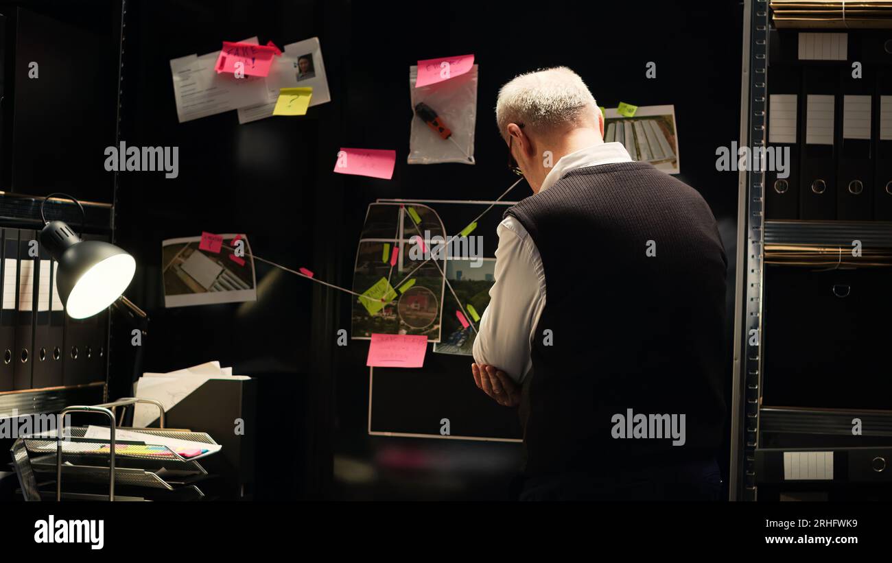 Private agent examine clues board to conduct criminal investigation, using classified documents to connect the dots in solving mystery. Law enforcement officer gathering evidence. Handheld shot. Stock Photo