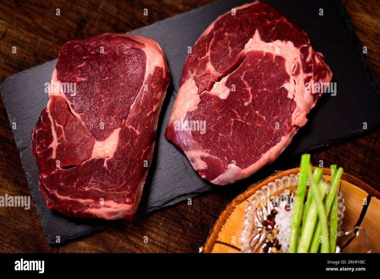 Two ribeye steaks with salt and pepper on the black cutting board