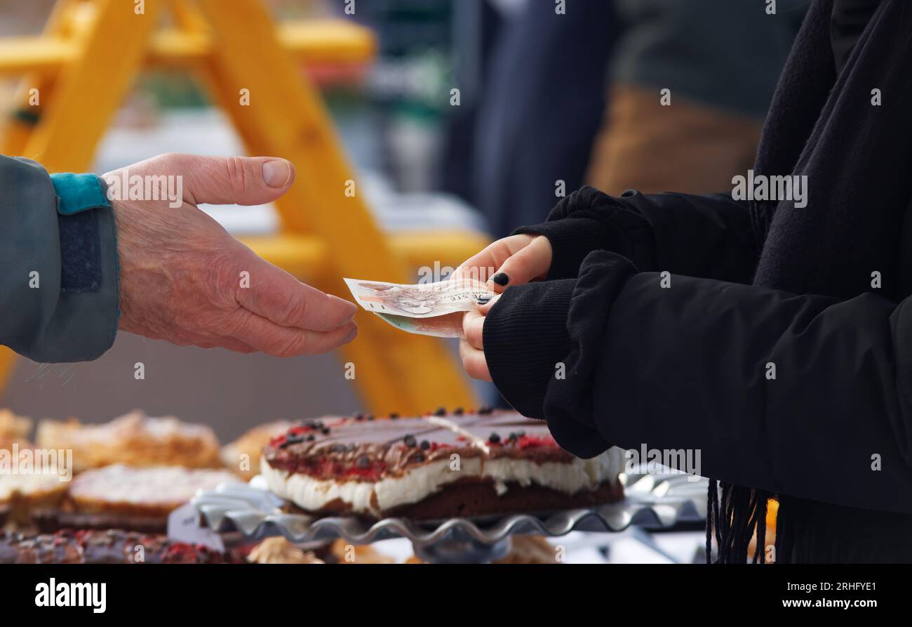At Prague farmers market, a customers outstretched hand exchanges money with a stallholder over a tempting array of pastries at a bustling bakery stal Stock Photo