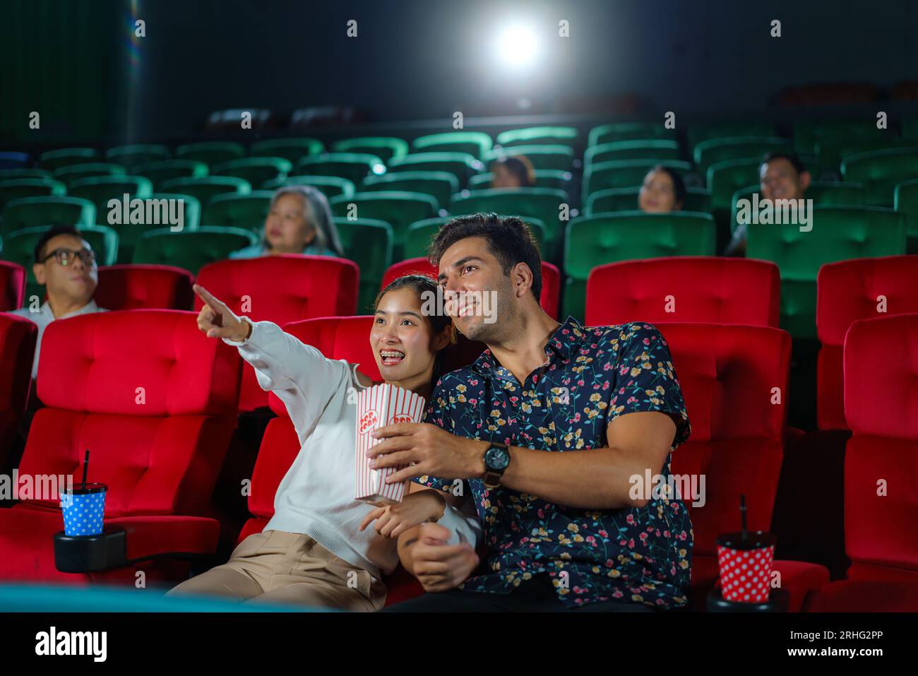 Couples enjoy movies while holding popcorn, creating a cozy and entertaining movie night experience at the cinema. Stock Photo