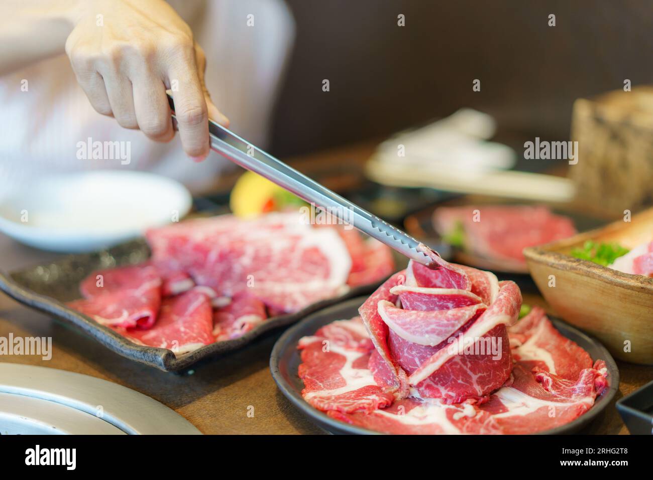 woman's hand employs tongs to place wagyu beef on a plate, ready to grill over charcoal, enhancing the dining experience at a Japanese restaurant Stock Photo