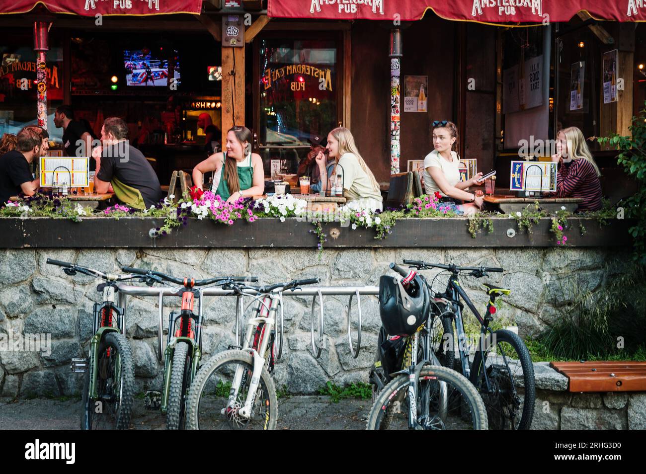 Tourists dine outside on a summer evening on restaurant patios with mountain bikes in the Whistler Village.  Whistler BC, Canada. Stock Photo