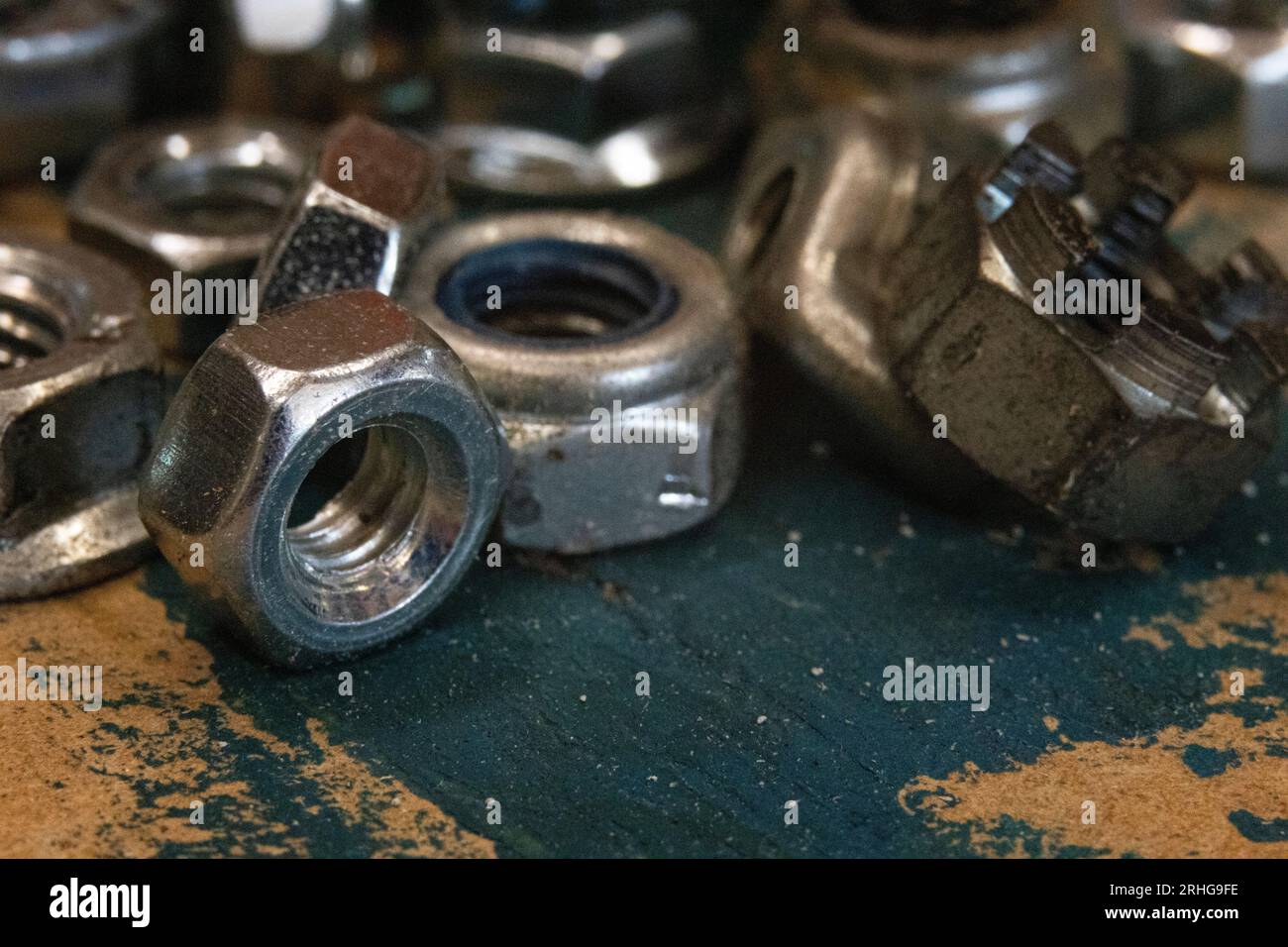 Industrial allure: A pile of metal nuts on an old workbench, accentuated by a smear of blue paint. Perfect for DIY, construction, or mechanical themes Stock Photo