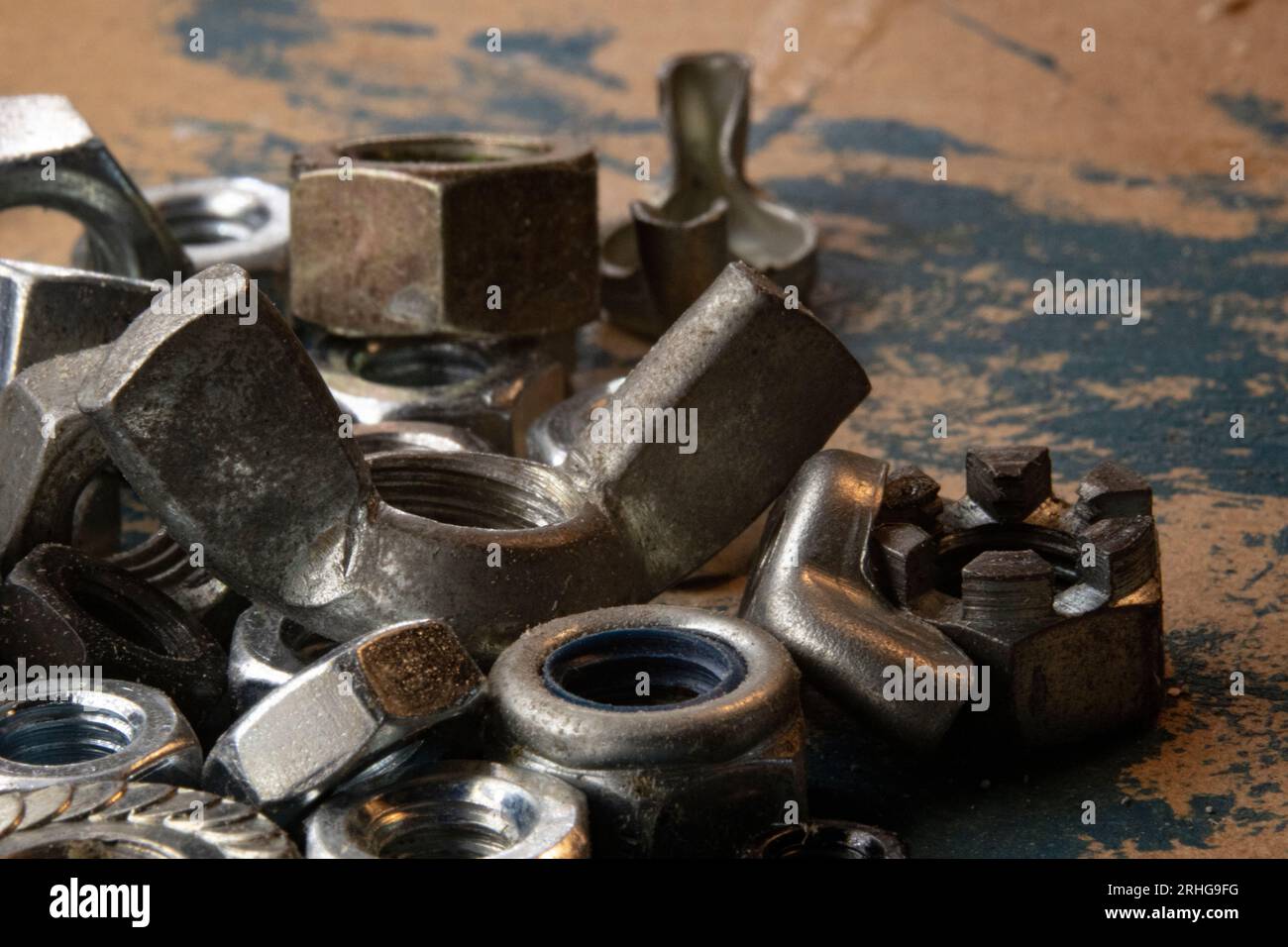 Industrial allure: A pile of metal nuts on an old workbench, accentuated by a smear of blue paint. Perfect for DIY, construction, or mechanical themes Stock Photo