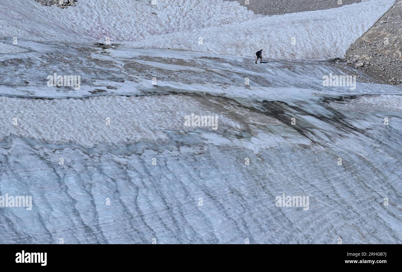 Grainau, Germany. 16th Aug, 2023. A hiker walks through the remnant snow of the Northern Schneeferner on the Zugspitzplatt. Researchers give them only a few more years: The last glaciers on German soil belong on the Red List. Credit: Angelika Warmuth/dpa/Alamy Live News Stock Photo