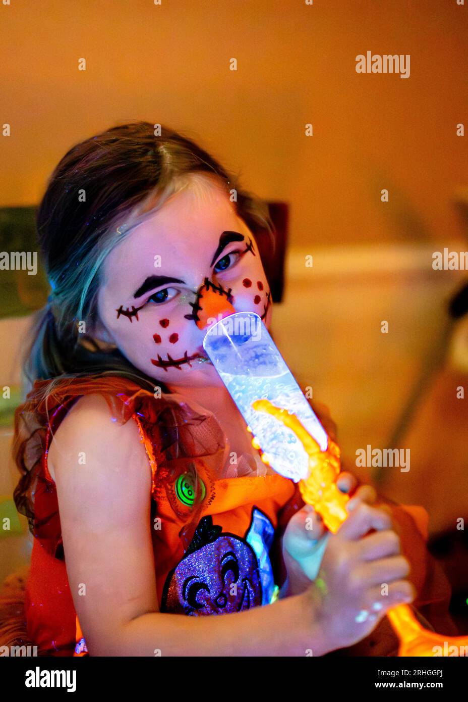 Kid drinking potion on Halloween scarecrow makeup face paint glowing in black light Stock Photo