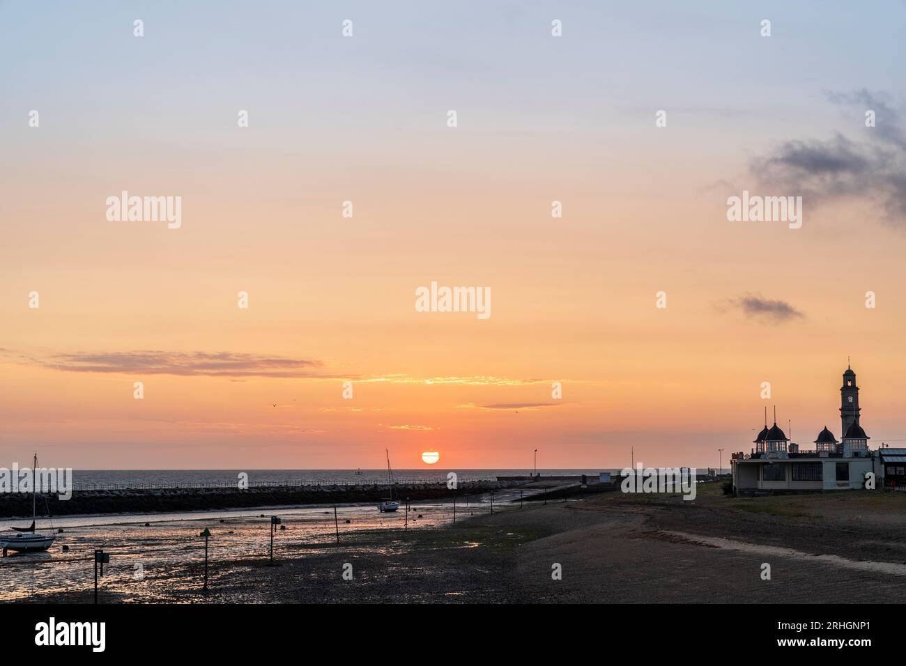 Sunrise into a orange sky over the single jetty of Herne bay harbour and the central bandstand with the distinctive clock tower behind, believed to be the oldest purpose built clock tower in the UK. The bandstand was designed by H. Kempton Dyson in 1924 and is build in the art deco style. Stock Photo