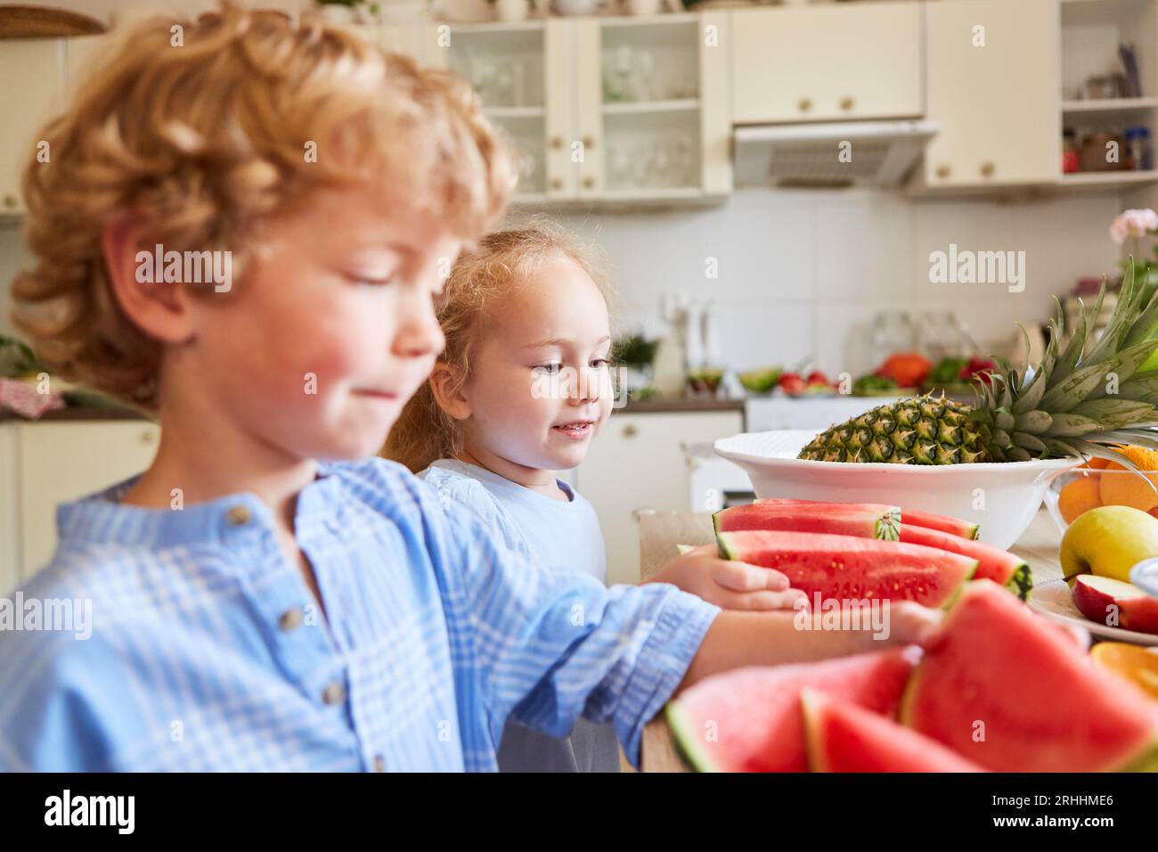 Sister choosing fresh watermelon slices with brother while standing in kitchen at home Stock Photo