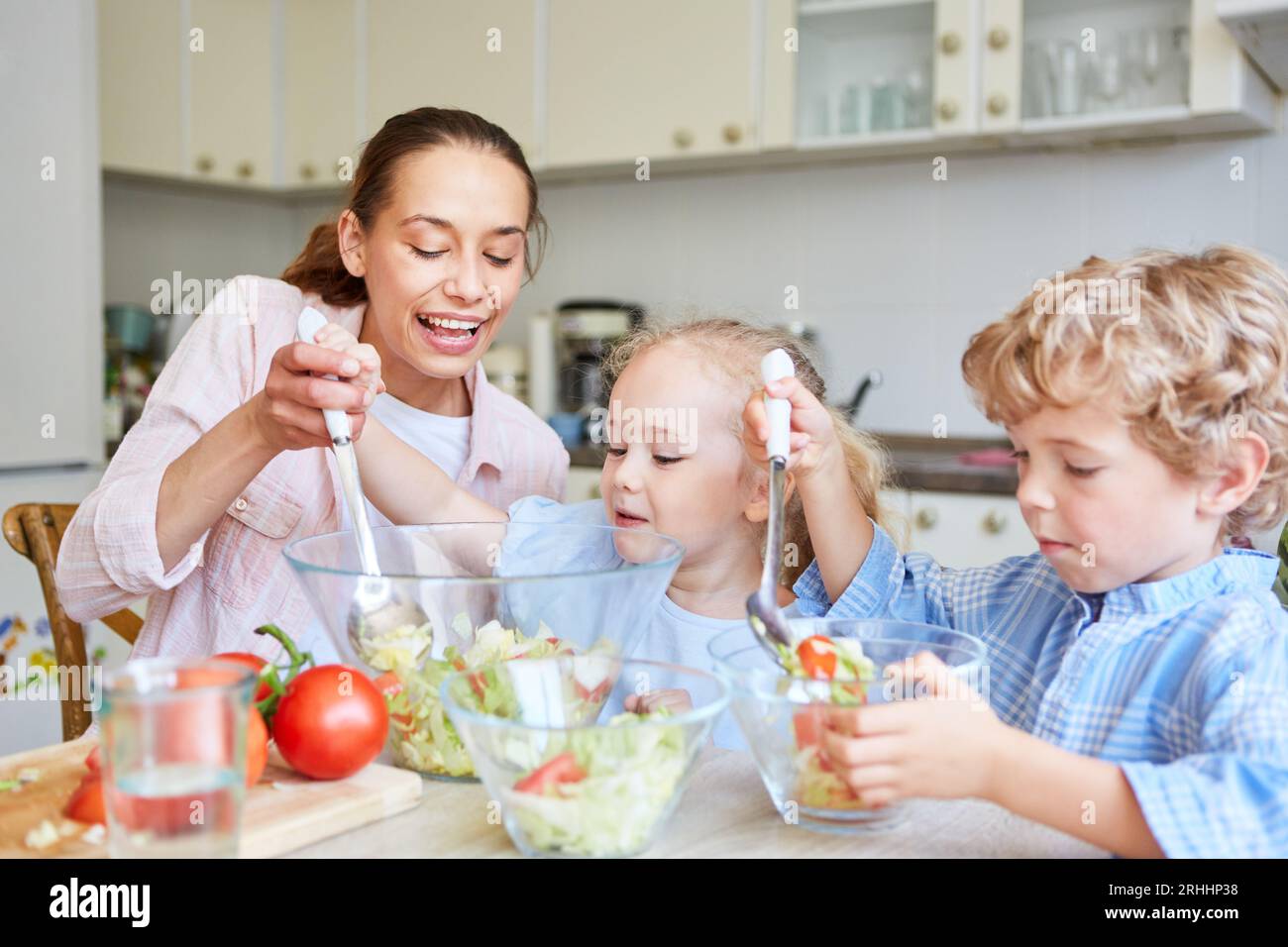 Happy mother helping daughter while making salad with brother in kitchen at home Stock Photo