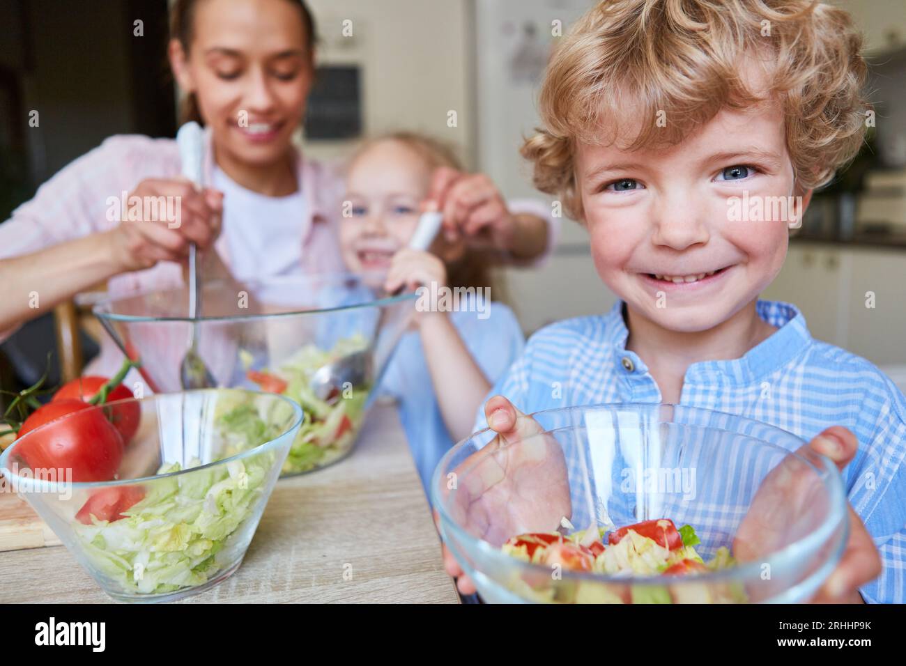 Portrait of smiling boy holding bowl with family preparing salad at home Stock Photo