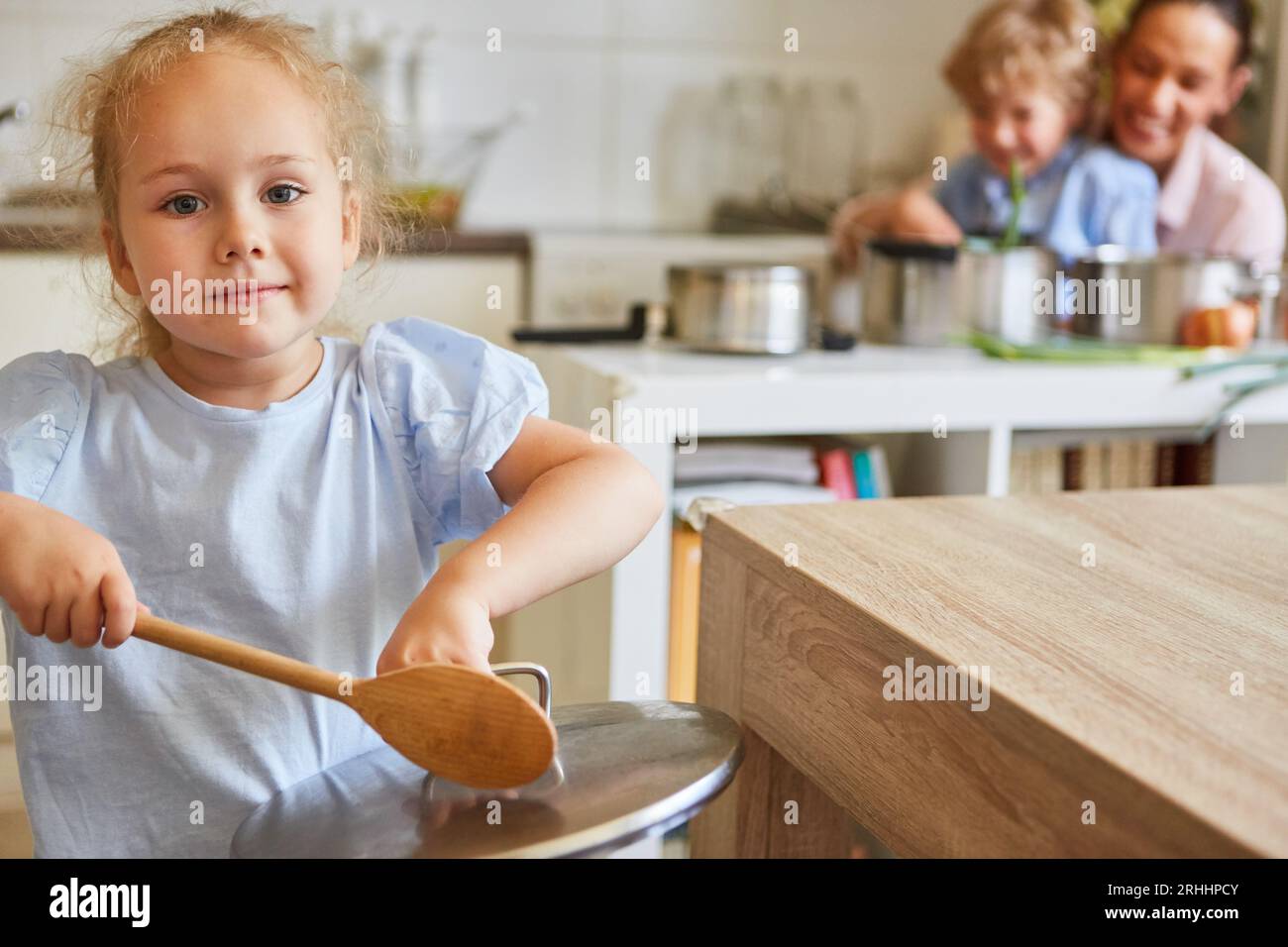 Portrait of girl banging lid with ladle while standing near table in kitchen at home Stock Photo