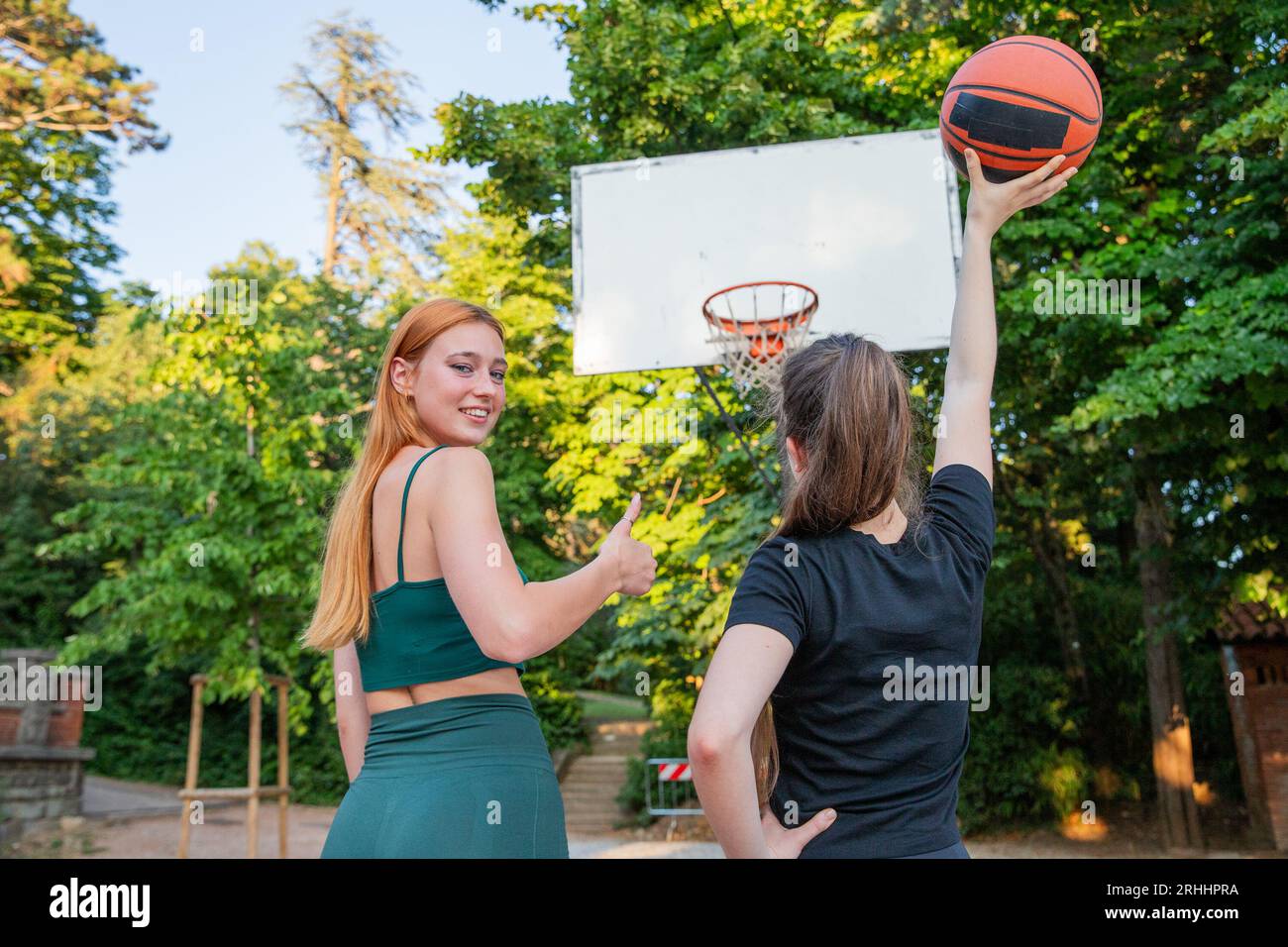 Two girls at the basketball court, one giving the thumbs up, the other holding the ball in her hand Stock Photo