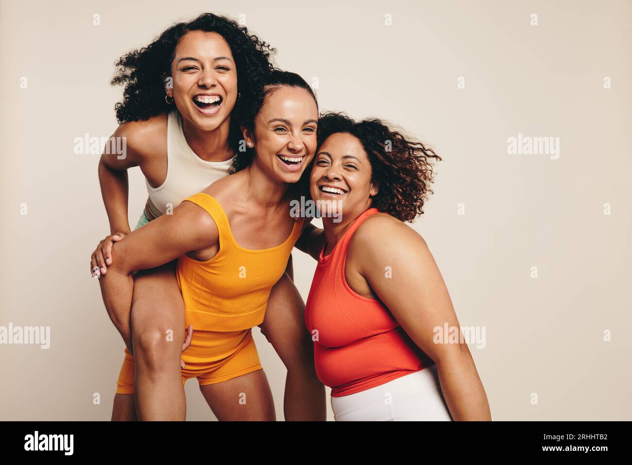 Happy female friends celebrate a healthy lifestyle through sports, exercise and fitness. Fit young women standing together in a studio, dressed in fit Stock Photo