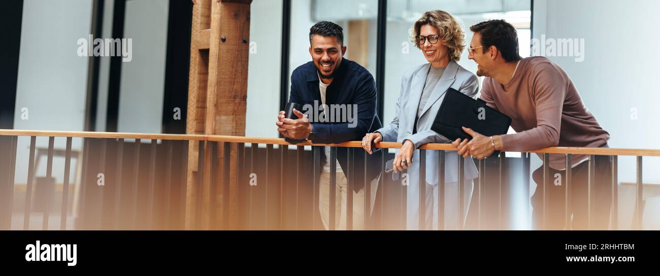 Creative design team stands on an interior balcony discussing ideas. Two business men and one business woman talk about their next project. Group of p Stock Photo