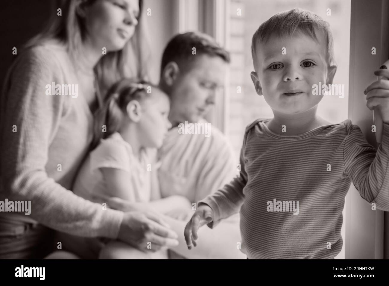cute caucasian little boy standing on window sill. His parents and ...