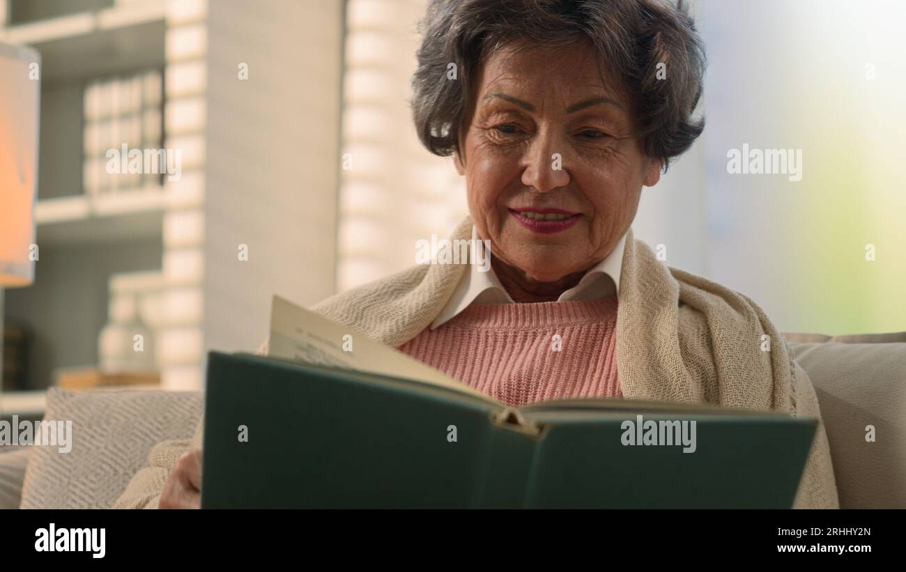 Happy inspired Caucasian old woman reading book smiling nostalgic senior mature lady elderly female retired pensioner grandmother read at home couch Stock Photo