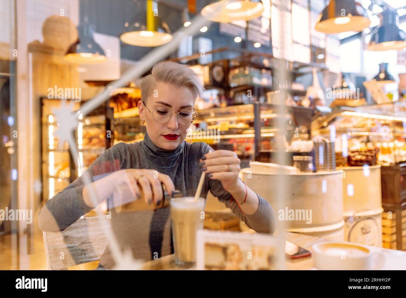 young short haired blond woman drinking latte at the table in cafe. High quality photo. Image with selective focuse and noise effect Stock Photo