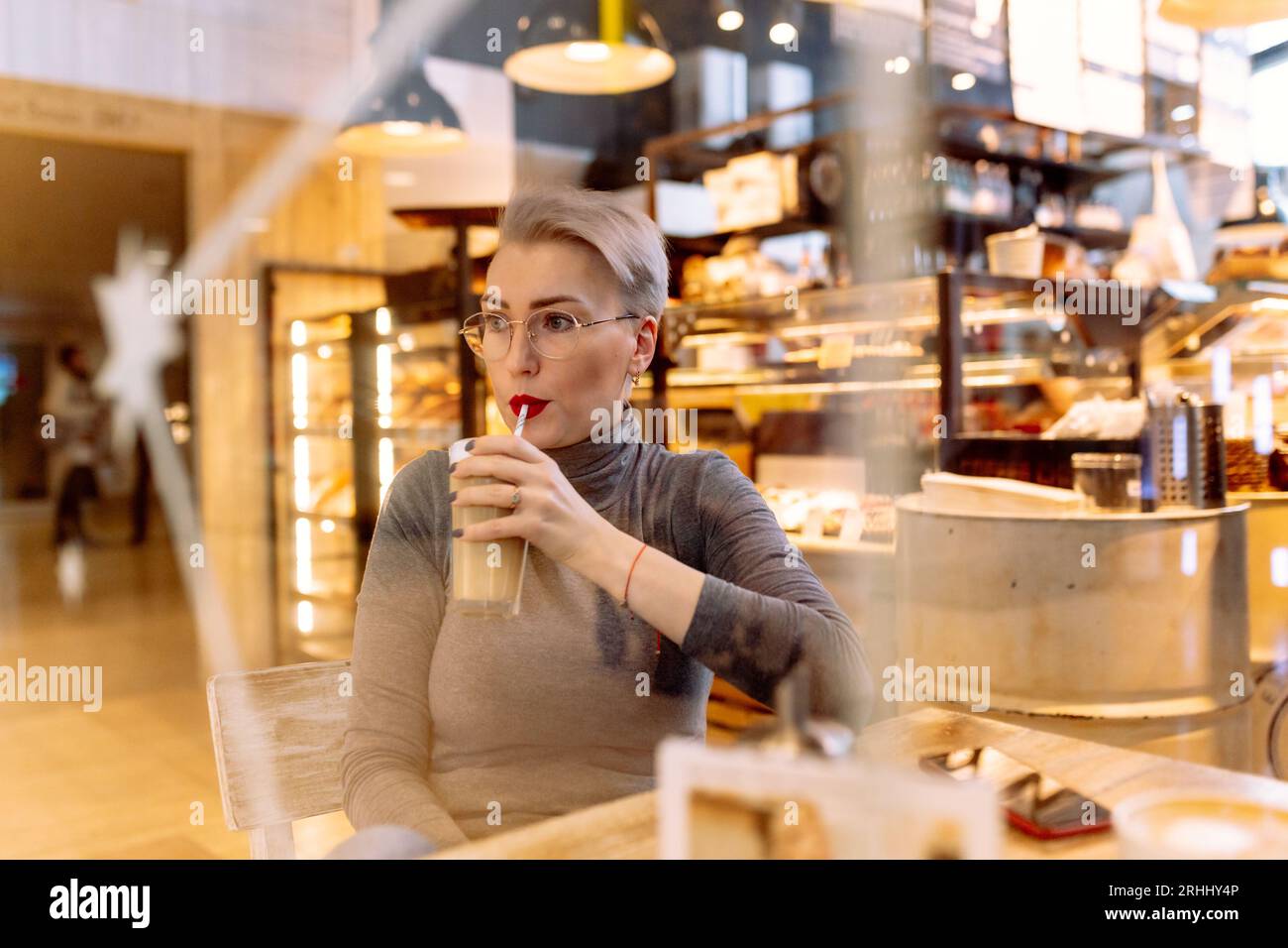 young short haired blond woman drinking latte at the table in cafe. High quality photo. Image with selective focuse and noise effect Stock Photo