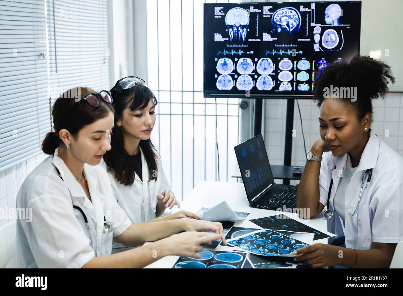 Team of female doctor check on scan results paper and looking at monitors in laboratory, share medical knowledge and experience benefits her coworkers Stock Photo