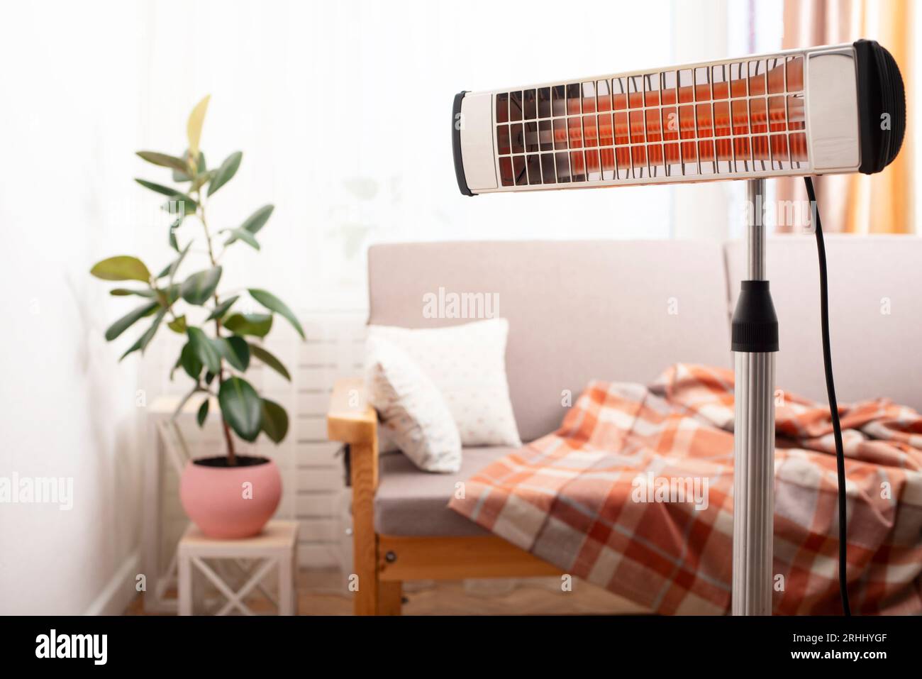 Electric infrared heater warming up living room with sofa and potted