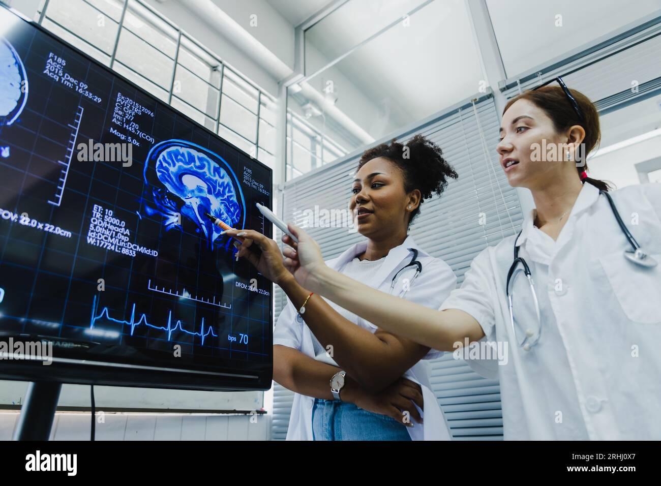 Team of female doctor check on scan results paper and looking at monitors in laboratory, share medical knowledge and experience benefits her coworkers Stock Photo