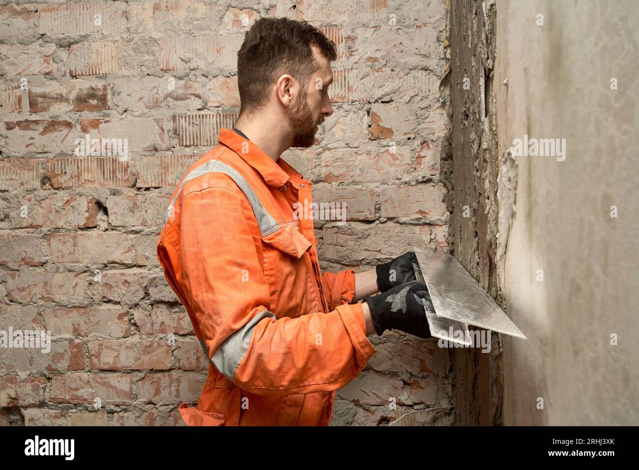 Man builder using h shape rule for plastering brick wall indoors. Stock Photo