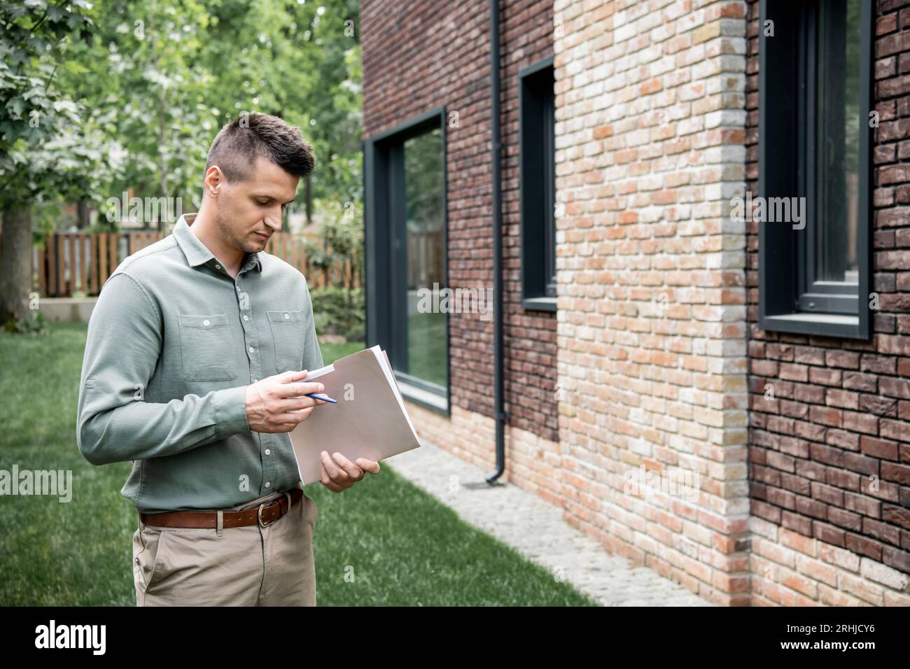 real estate agent holding folder and pen while standing near contemporary building on city street Stock Photo