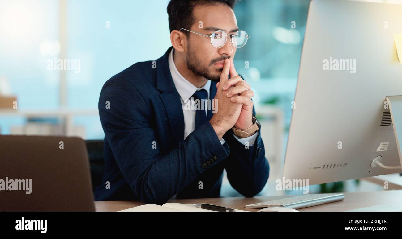 Thinking IT manager working on a desktop computer and laptop in a modern office. Information Technology software engineer analyzing data management Stock Photo