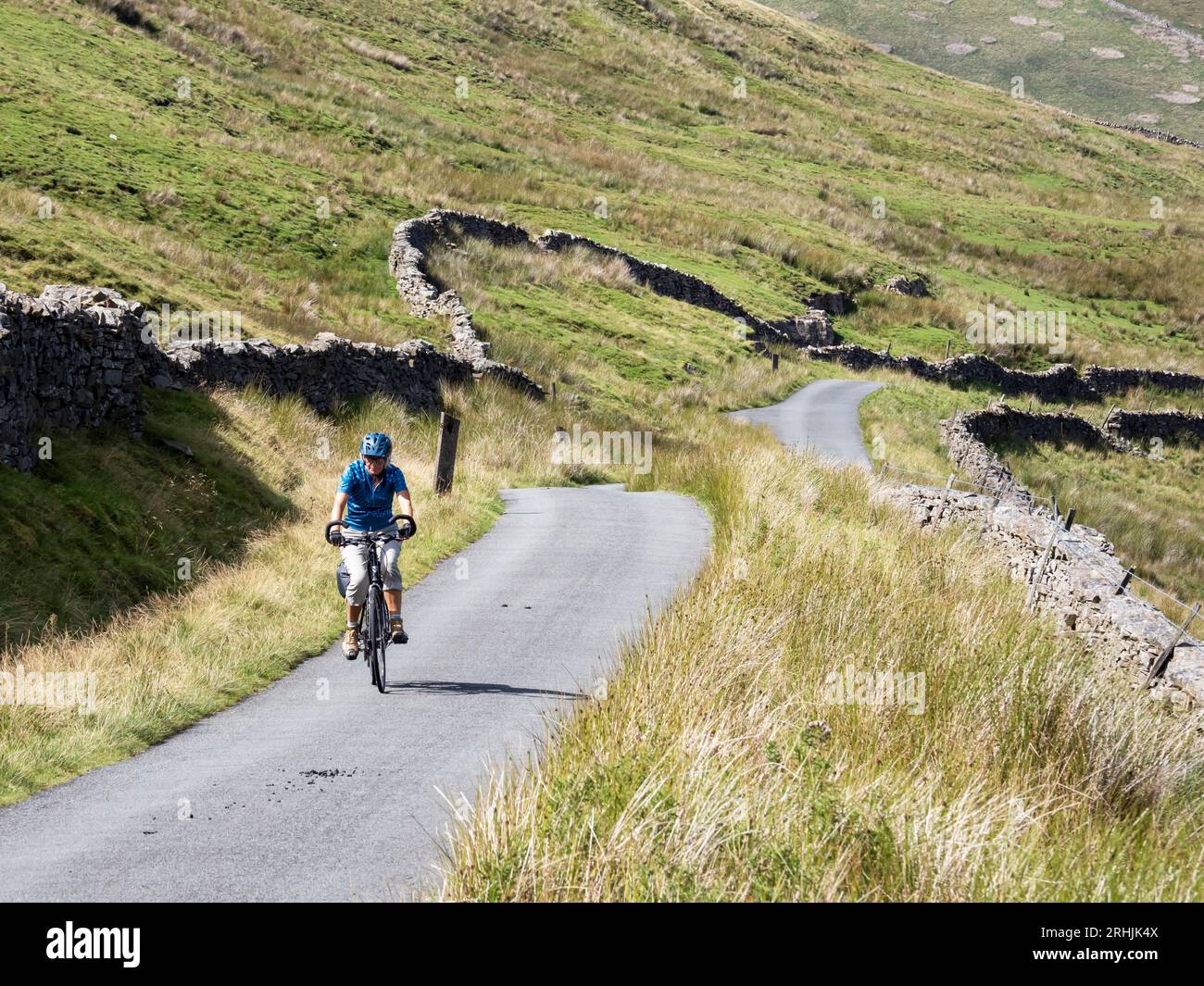 A woman cycling up the steep pass to White Shaw Moss between Deepdale and Kingsdale, Yorkshire Dales, UK. Stock Photo