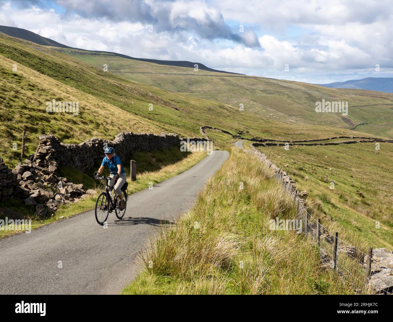 A woman cycling up the steep pass to White Shaw Moss between Deepdale and Kingsdale, Yorkshire Dales, UK. Stock Photo