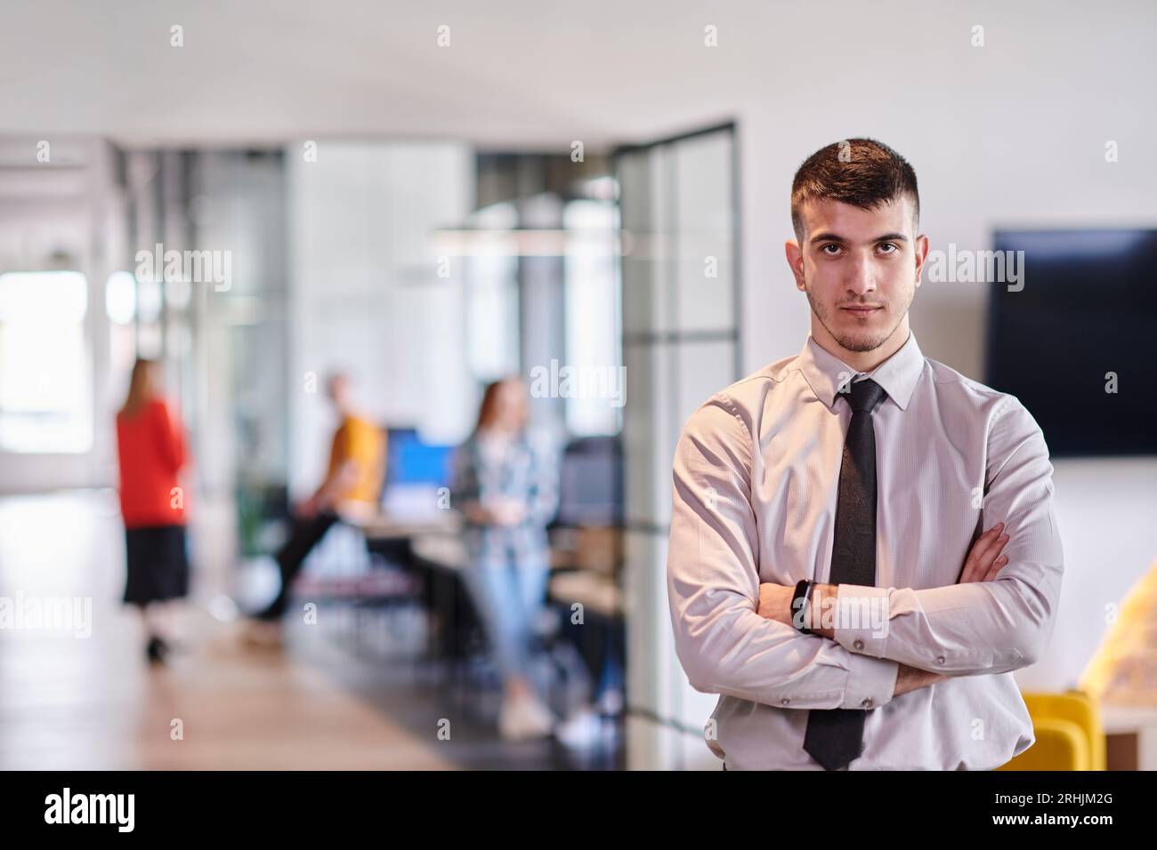A young business leader stands with crossed arms in a modern office ...
