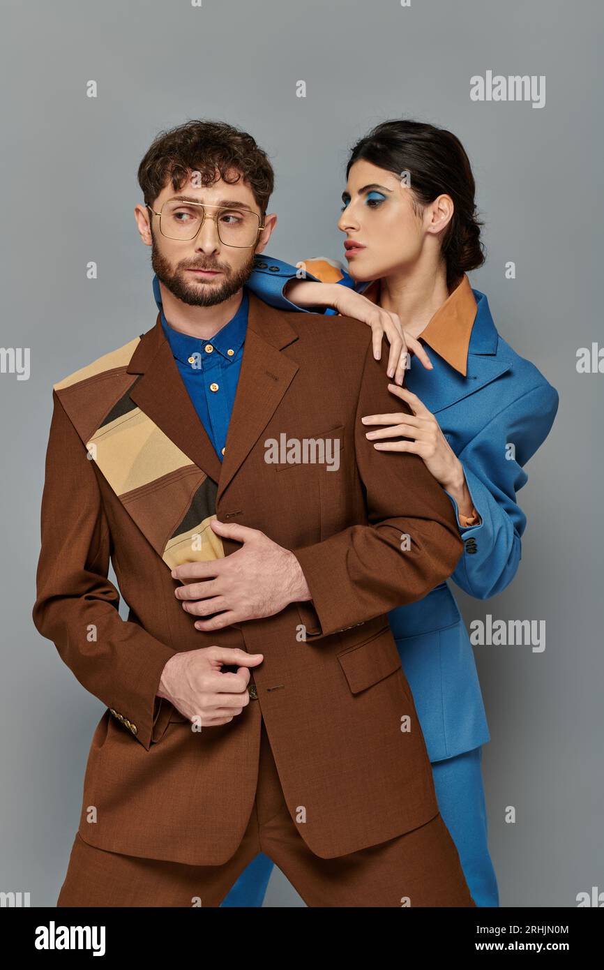 stylish man and woman in suits posing on grey background, elegant style ...