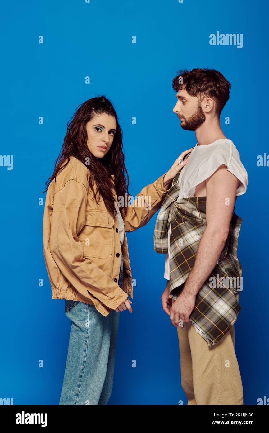 fashionable couple, casual attire, blue backdrop, woman touching chest of bearded man, bold makeup Stock Photo