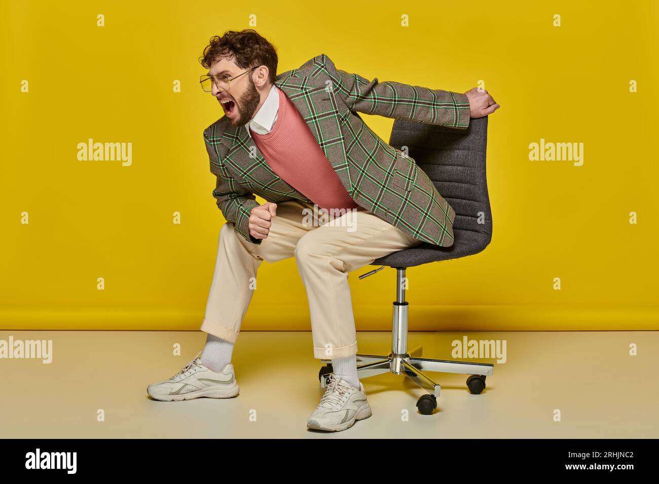 emotional and bearded man screaming and sitting on office chair, yellow