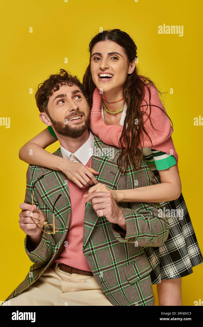 excited woman hugging bearded man, holding glasses, yellow backdrop, college outfits, students Stock Photo