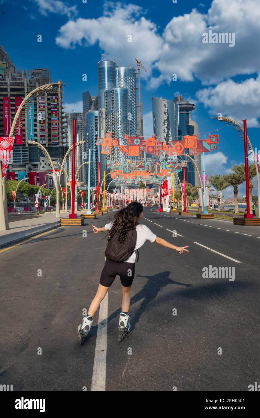 Against the backdrop of Qatar's 2022 FIFA World Cup, a spirited fan glides gracefully on her skating shoes along the road adjacent to the bustling Cor Stock Photo