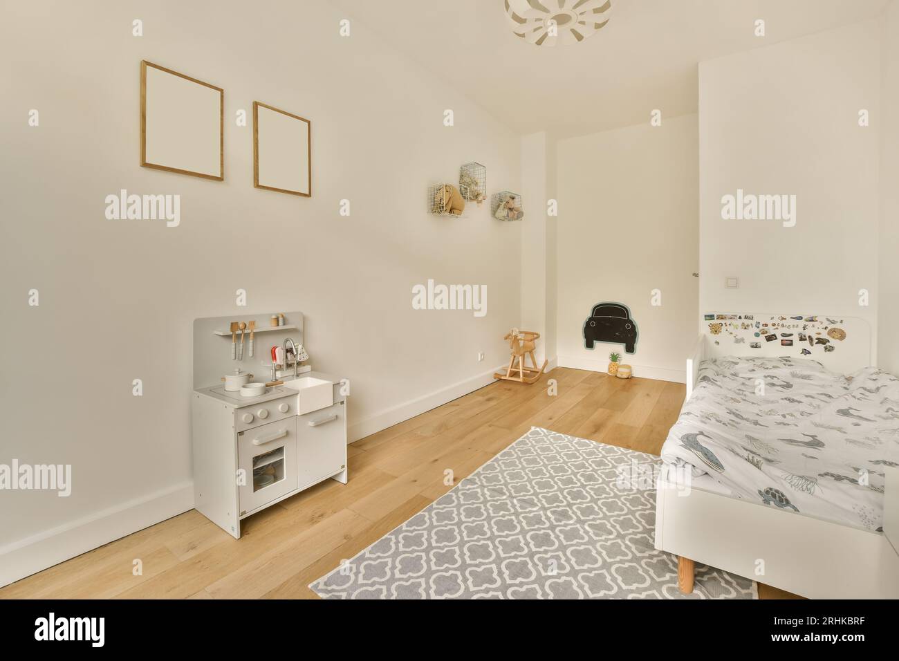 a child's room with white walls and hardwood flooring, including a grey patterned rug on the floor Stock Photo