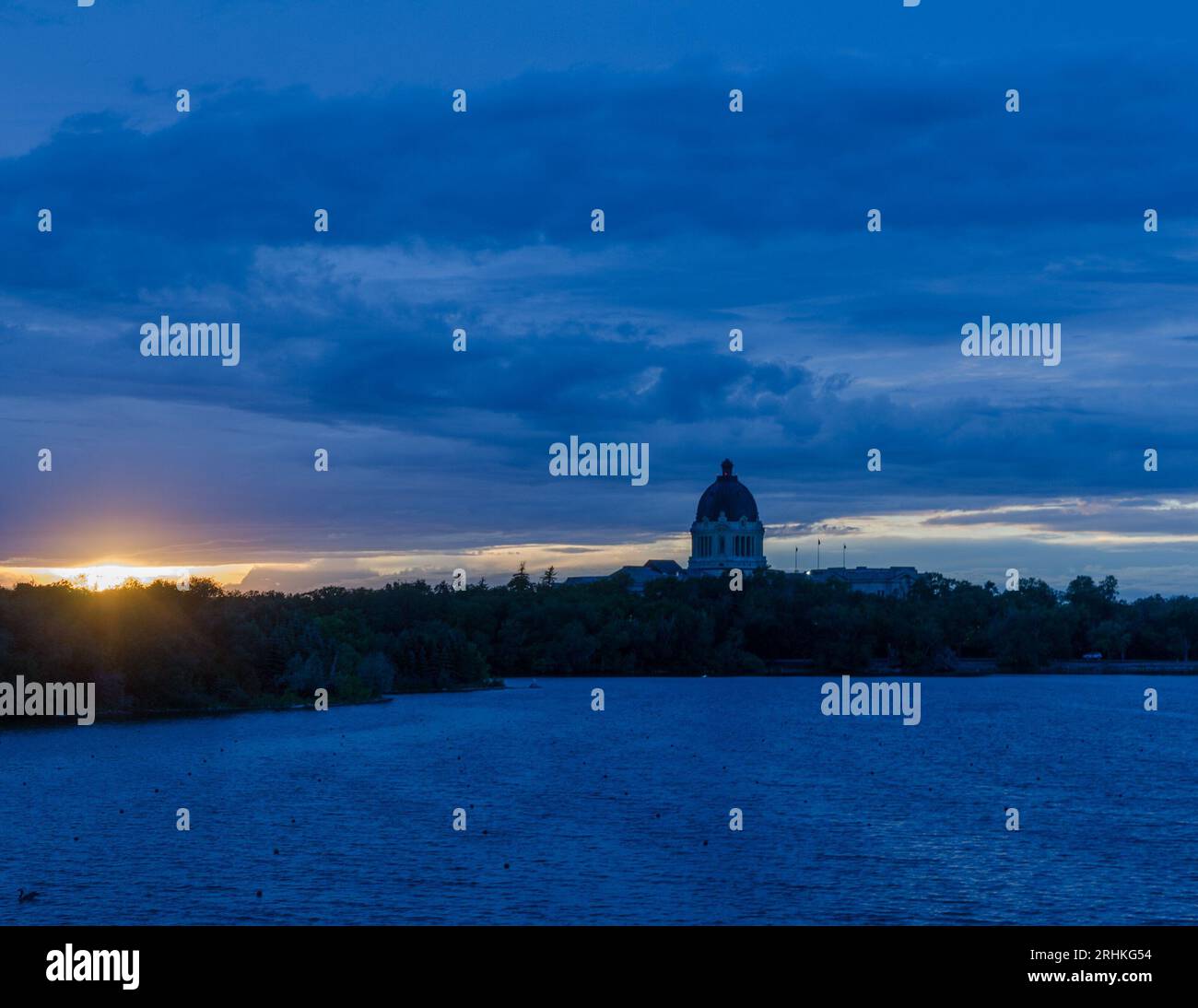 The dome of the Saskatchewan provincial legislative building can be seen with a backdrop of a prairie sunset. Wascana Lake is in the foreground. Stock Photo