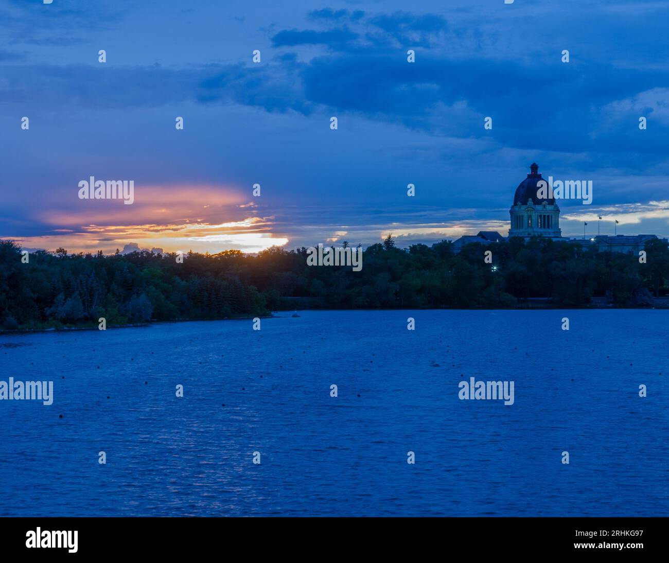 The dome of the Saskatchewan provincial legislative building can be seen with a backdrop of a prairie sunset. Wascana Lake is in the foreground. Stock Photo