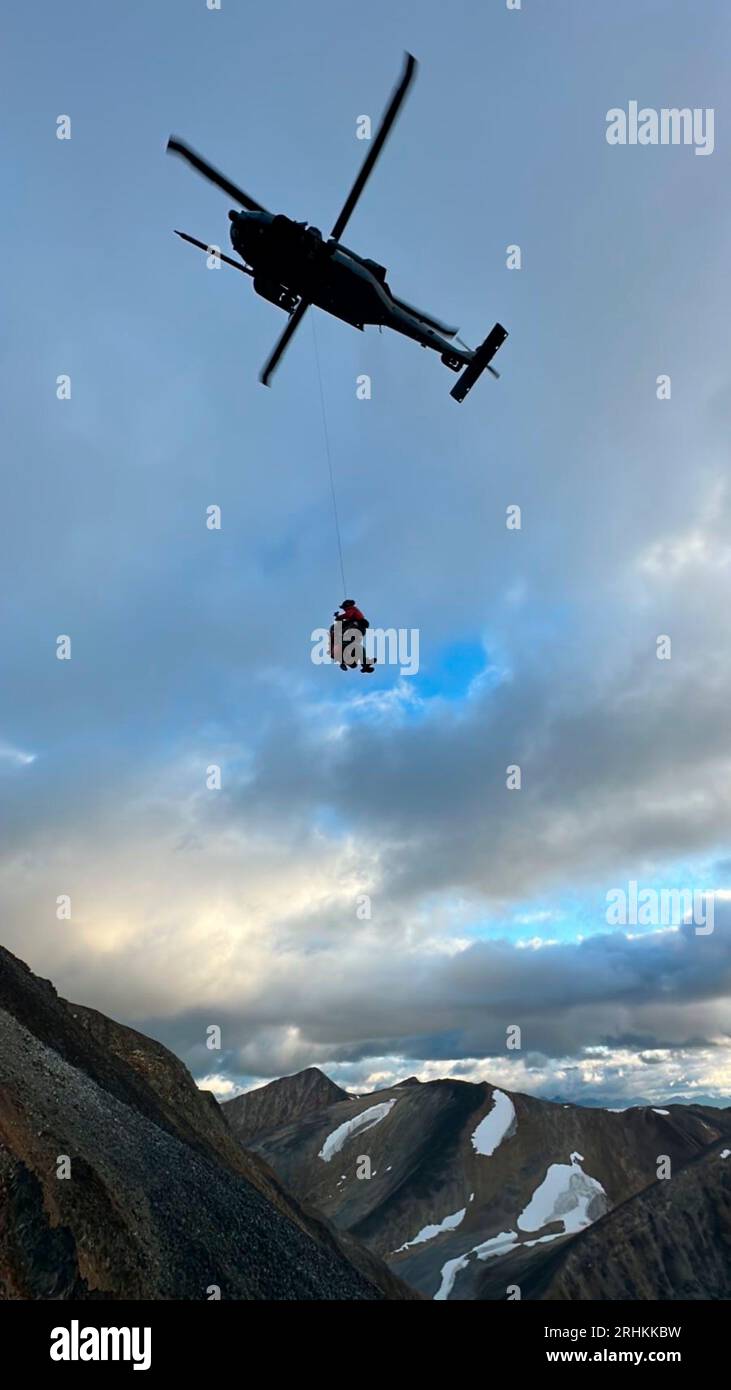 Tonsina, United States. 11 August, 2023. U.S. Air Force Staff Sgt. Nathan Weltman, a pararescueman with 57th Rescue Squadron, hoists a stranded sheep hunter from a cliff face in the remote Tonsina Controlled Use Area, August 11, 2023 near Tonsina, Alaska. Two hunters were rescued from a 6,000-foot-high cliff after becoming stranded.  Credit: Alaska Guards/US Air Force/Alamy Live News Stock Photo