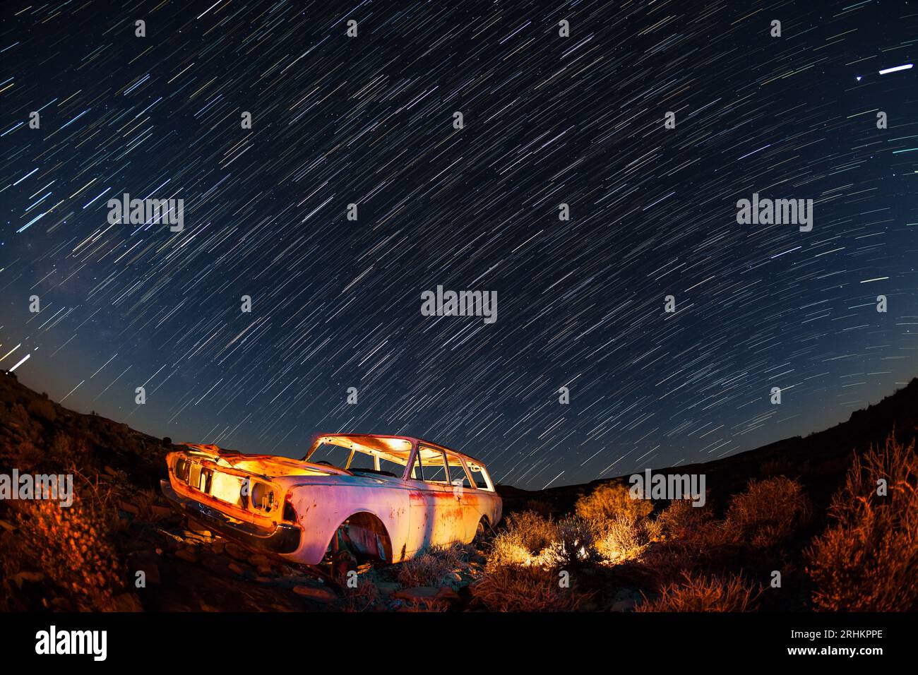 Night photograph of illuminated old car wreck in foreground with a sky filled with star trails photography techniques in Karoo, South Africa Stock Photo