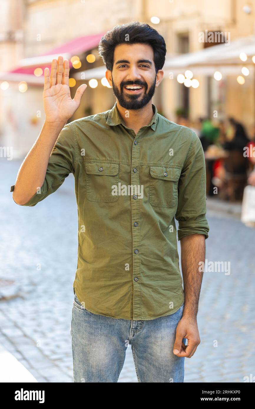 Bearded indian man smiling friendly at camera, waving hands gesturing