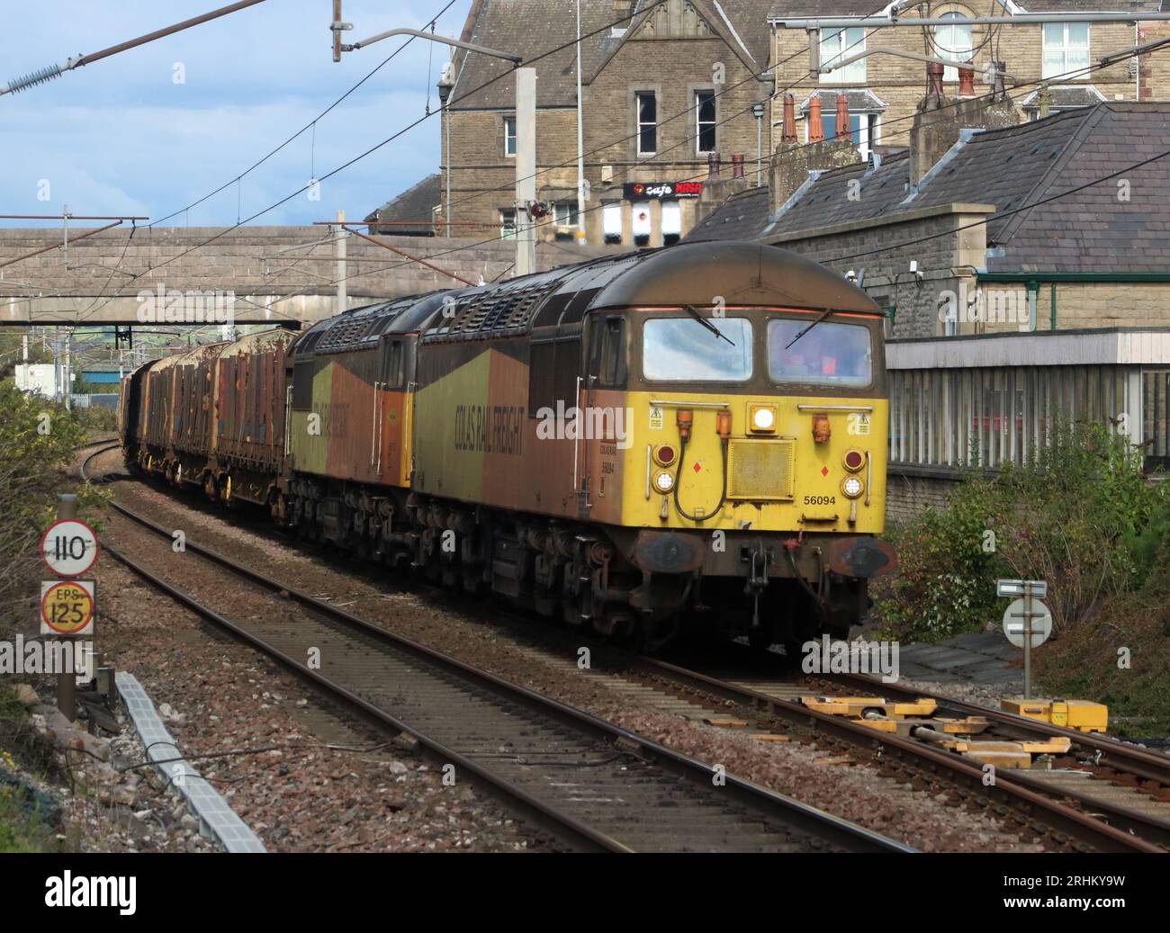 Two Colas Rail Freight liveried class 56 diesel-electric locos double-head log train through Carnforth on West Coast Main Line, 16th August 2023. Stock Photo