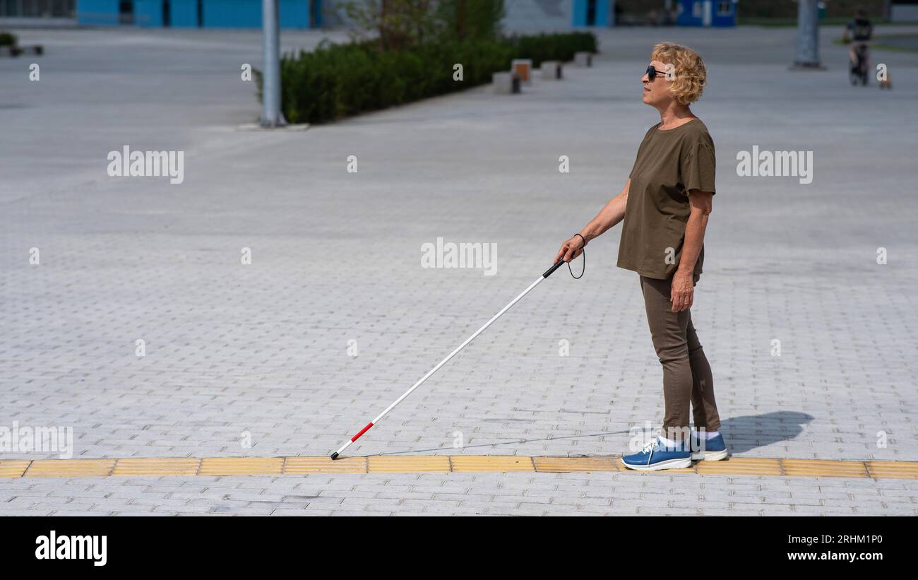 An elderly blind woman walks with a cane along a tactile tile Stock